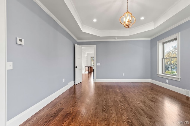 empty room with a tray ceiling, a chandelier, dark hardwood / wood-style floors, and ornamental molding