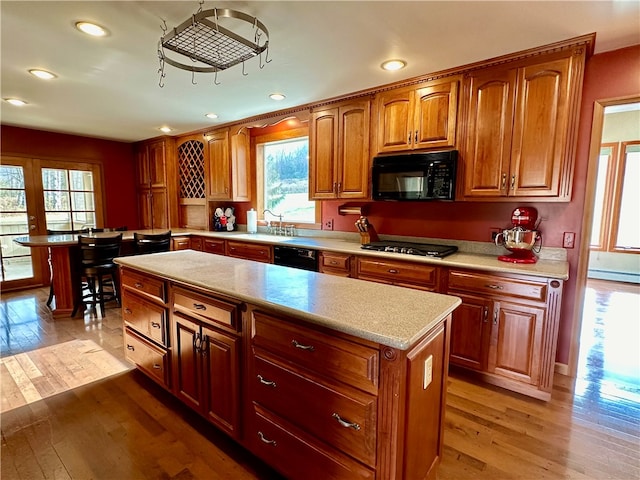 kitchen with light hardwood / wood-style flooring, a center island, a baseboard heating unit, and black appliances