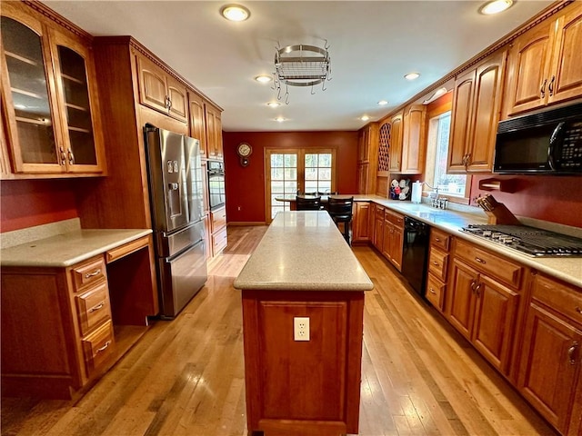 kitchen featuring a kitchen island, glass insert cabinets, light countertops, black appliances, and a sink