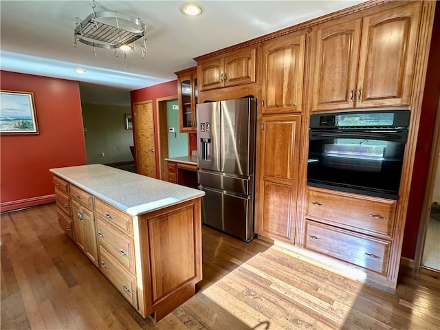 kitchen with brown cabinetry, glass insert cabinets, light countertops, stainless steel refrigerator with ice dispenser, and black oven