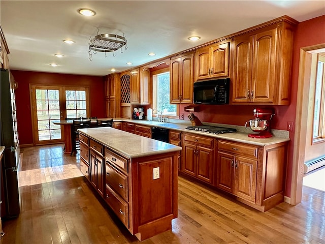 kitchen with a baseboard radiator, black appliances, light hardwood / wood-style flooring, and a kitchen island