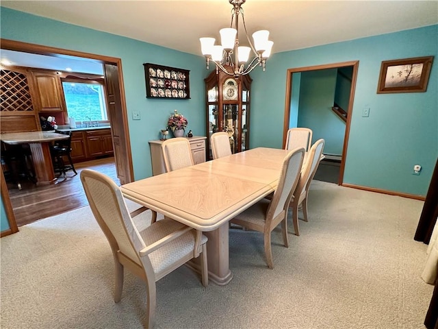 dining space with a chandelier, baseboard heating, light carpet, and baseboards