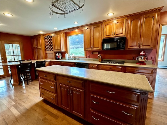 kitchen with baseboard heating, sink, black appliances, a center island, and light hardwood / wood-style floors