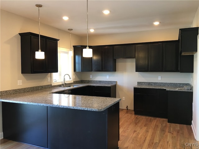 kitchen with sink, kitchen peninsula, pendant lighting, and light hardwood / wood-style floors