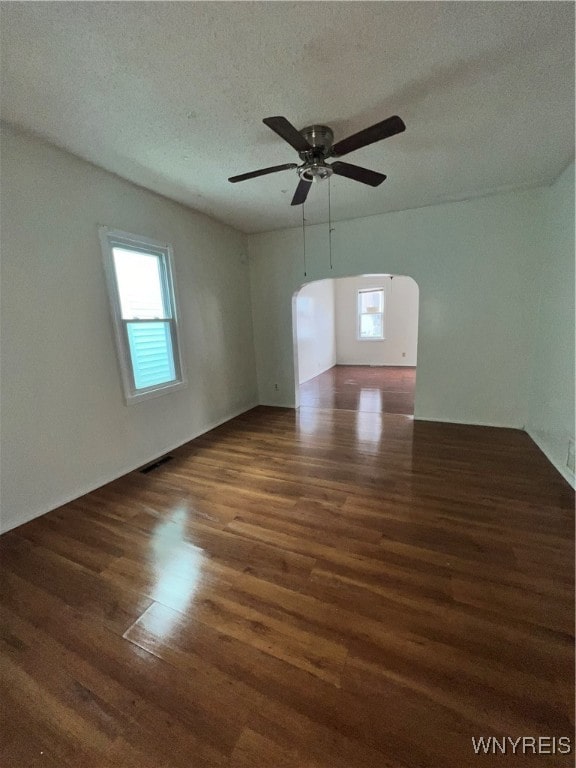 empty room with ceiling fan, a wealth of natural light, a textured ceiling, and dark hardwood / wood-style floors