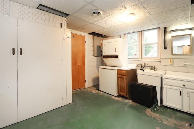 basement with white fridge, a drop ceiling, stacked washer and clothes dryer, and sink