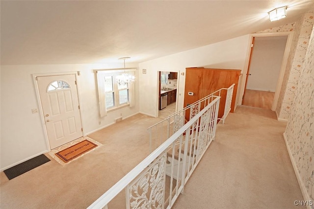 hall featuring lofted ceiling, light carpet, and a chandelier