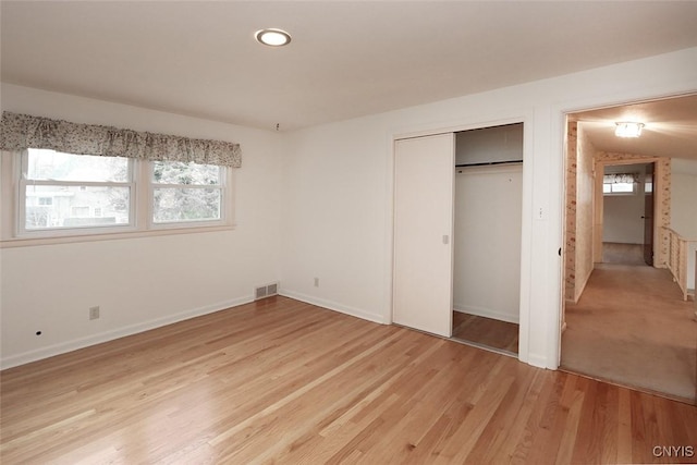 unfurnished bedroom featuring light wood-type flooring, a closet, and multiple windows