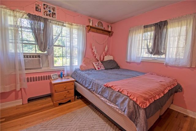 bedroom with cooling unit, hardwood / wood-style flooring, and radiator