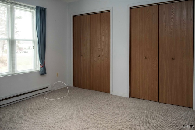 unfurnished bedroom with light carpet, a baseboard heating unit, and two closets