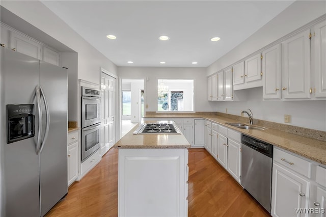 kitchen featuring sink, a kitchen island, light hardwood / wood-style floors, stainless steel appliances, and white cabinets