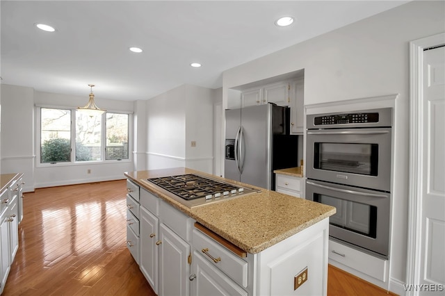 kitchen with appliances with stainless steel finishes, light wood-type flooring, a kitchen island, hanging light fixtures, and white cabinetry