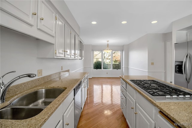 kitchen featuring sink, hanging light fixtures, stainless steel appliances, white cabinets, and light hardwood / wood-style flooring