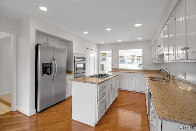 kitchen with appliances with stainless steel finishes, sink, a kitchen island, light hardwood / wood-style floors, and white cabinets