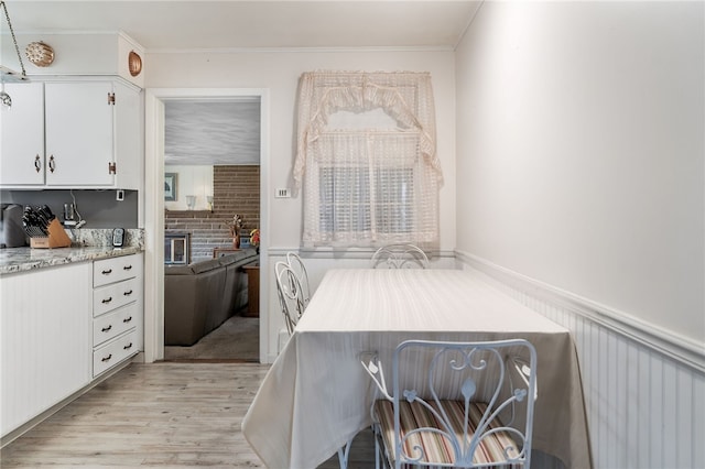 kitchen with white cabinets, light wood-type flooring, light stone countertops, and crown molding