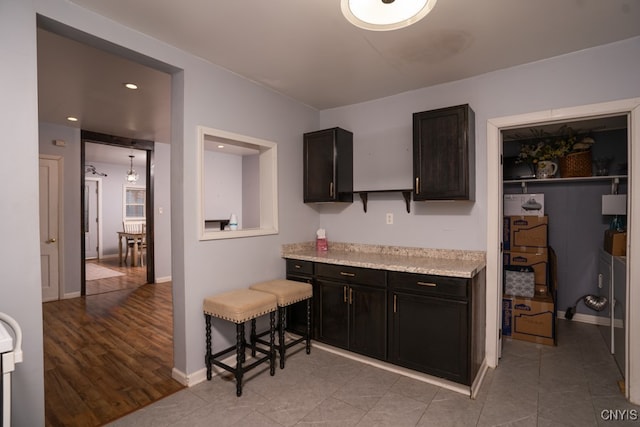 kitchen with a kitchen breakfast bar, light stone counters, dark brown cabinets, and light wood-type flooring