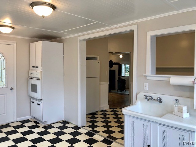 kitchen featuring crown molding, white cabinetry, sink, and white appliances