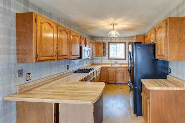 kitchen featuring tasteful backsplash, stainless steel appliances, decorative light fixtures, sink, and kitchen peninsula