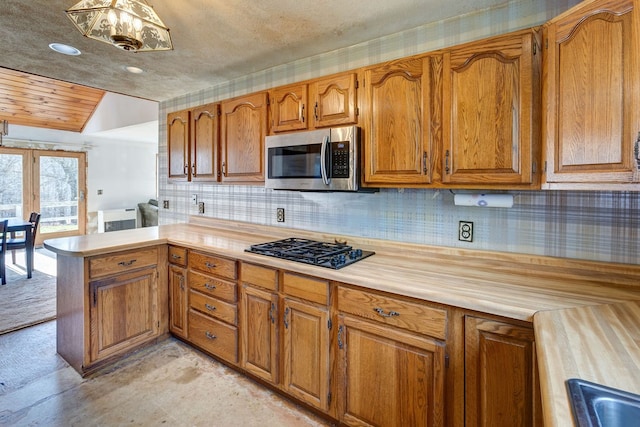 kitchen featuring vaulted ceiling, kitchen peninsula, gas stovetop, a textured ceiling, and tasteful backsplash