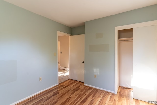 unfurnished bedroom featuring baseboard heating, a closet, and light wood-type flooring