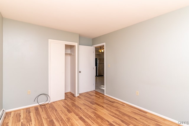 unfurnished bedroom with a closet, a baseboard heating unit, light wood-type flooring, and stainless steel refrigerator