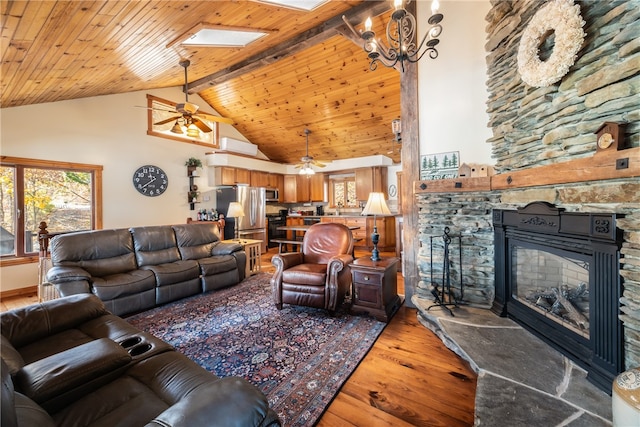 living room with a skylight, a stone fireplace, hardwood / wood-style floors, beam ceiling, and high vaulted ceiling