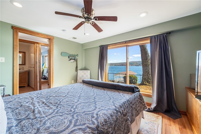 bedroom featuring ensuite bathroom, access to outside, light wood-type flooring, ceiling fan, and a water view