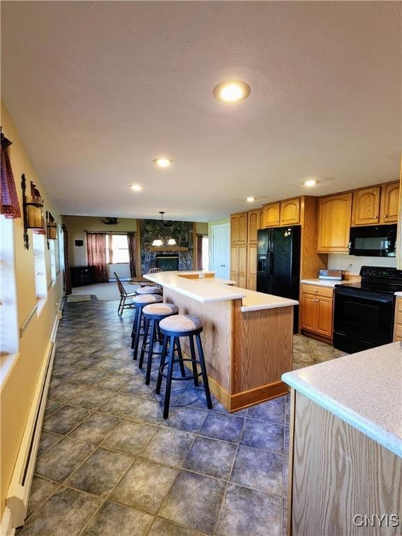 kitchen with a kitchen island, a baseboard heating unit, black appliances, a stone fireplace, and a breakfast bar area