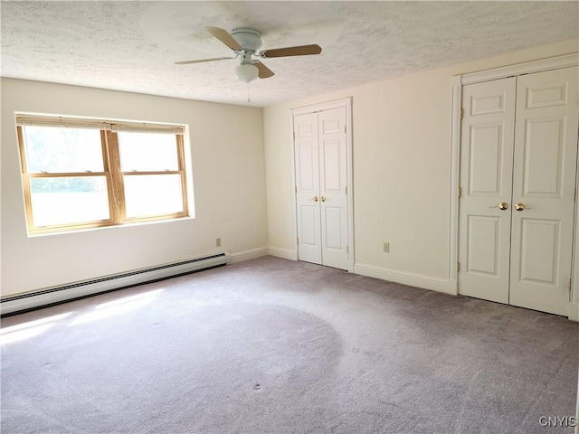 unfurnished bedroom with a baseboard heating unit, ceiling fan, a textured ceiling, light colored carpet, and multiple closets