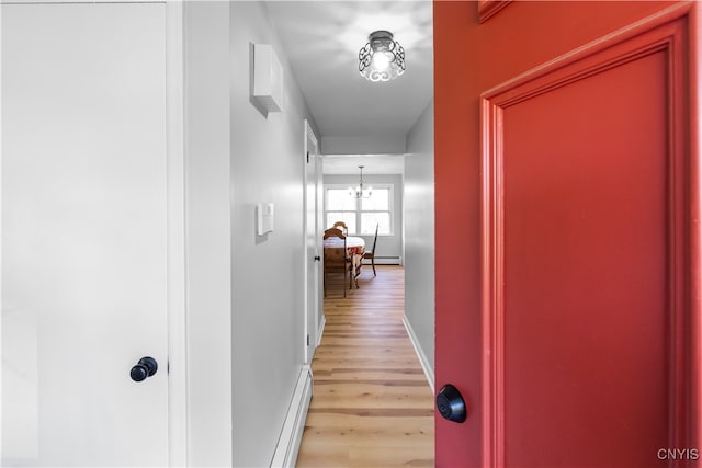 corridor featuring light hardwood / wood-style floors, a baseboard radiator, and a notable chandelier