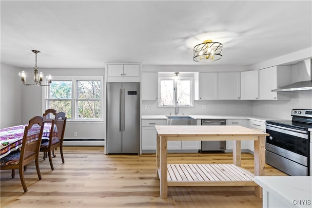 kitchen with stainless steel appliances, white cabinetry, an inviting chandelier, wall chimney range hood, and light wood-type flooring