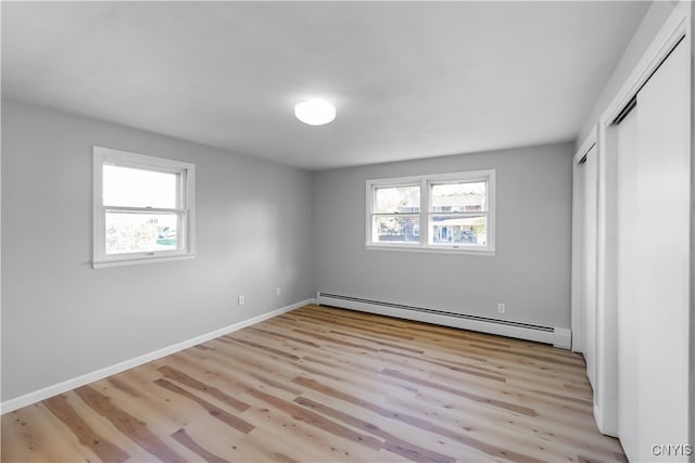 unfurnished bedroom featuring light hardwood / wood-style flooring, multiple windows, and a baseboard heating unit