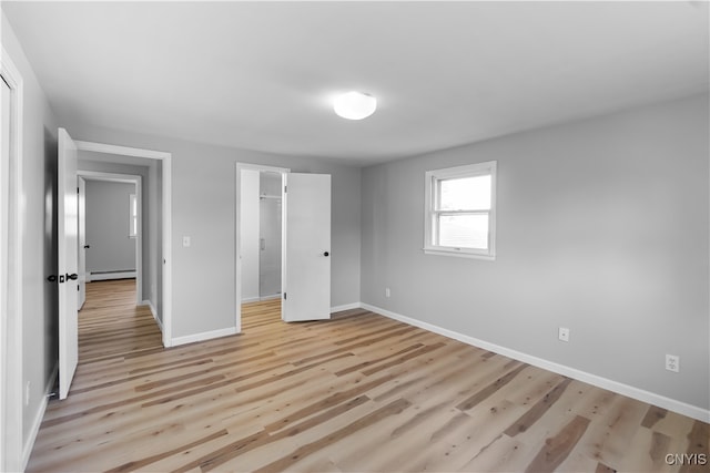 unfurnished bedroom with a closet, a spacious closet, light hardwood / wood-style floors, and a baseboard heating unit