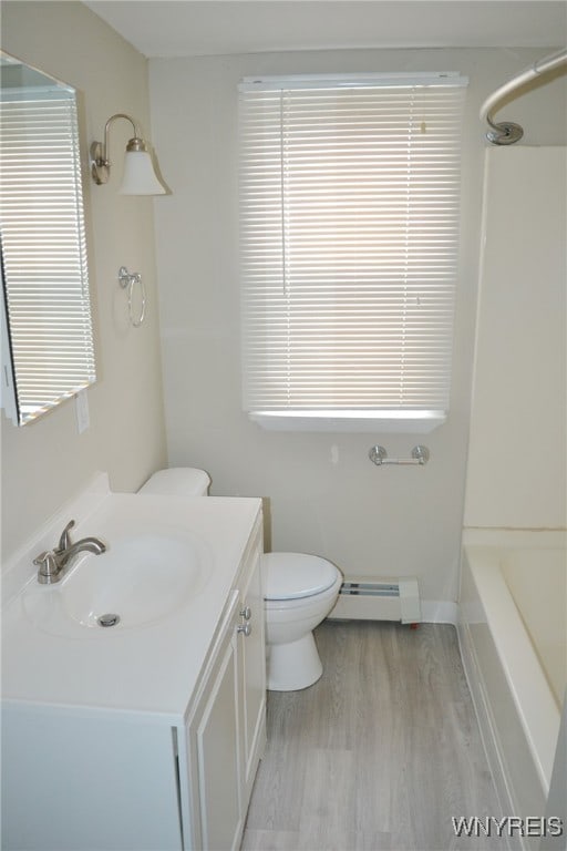 full bathroom featuring vanity, wood-type flooring, a baseboard radiator, washtub / shower combination, and toilet