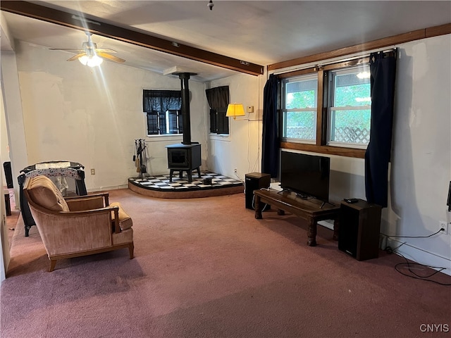 carpeted living room with beam ceiling, a wood stove, and ceiling fan