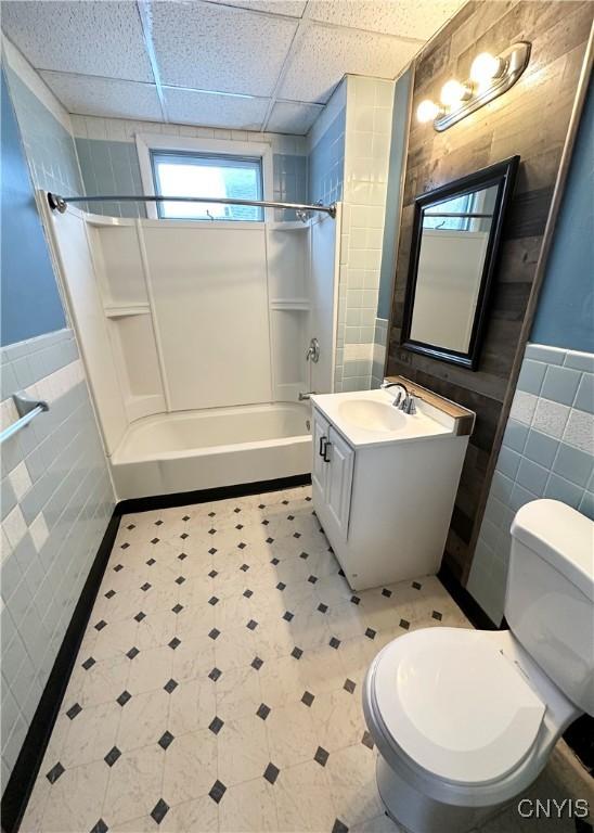 full bathroom featuring a paneled ceiling, bathing tub / shower combination, tile walls, vanity, and toilet