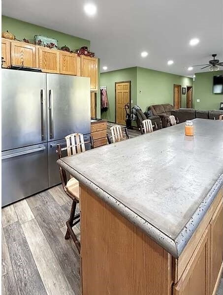 kitchen with a kitchen island, stainless steel refrigerator, a kitchen breakfast bar, ceiling fan, and light hardwood / wood-style flooring