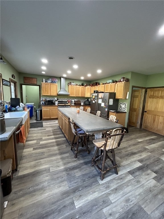 kitchen featuring appliances with stainless steel finishes, wall chimney exhaust hood, backsplash, and light hardwood / wood-style flooring