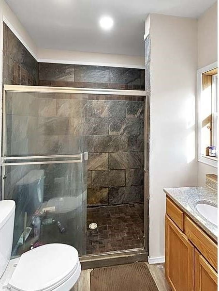 bathroom featuring hardwood / wood-style floors, a shower with shower door, vanity, and toilet