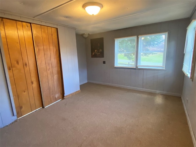 unfurnished bedroom featuring a closet, wooden walls, and light colored carpet