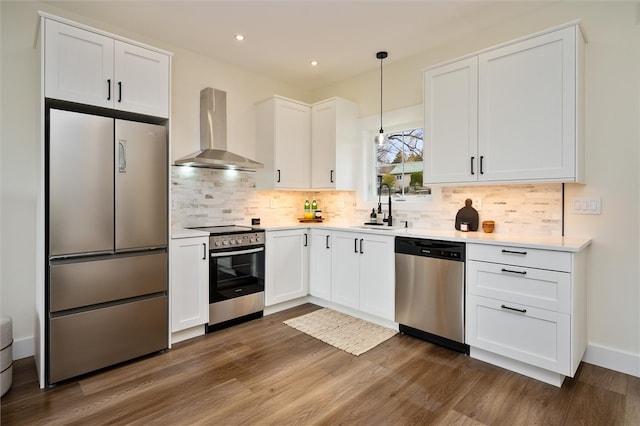 kitchen featuring white cabinetry, wall chimney exhaust hood, pendant lighting, and appliances with stainless steel finishes