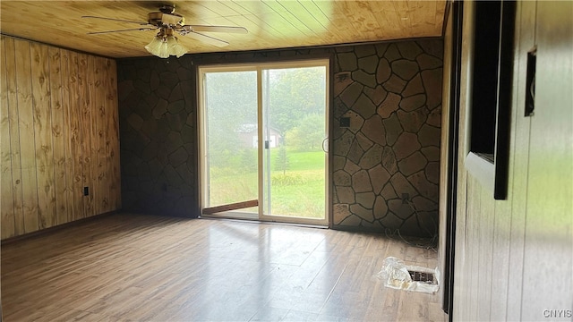 unfurnished room featuring light wood-type flooring, wood walls, ceiling fan, and wooden ceiling