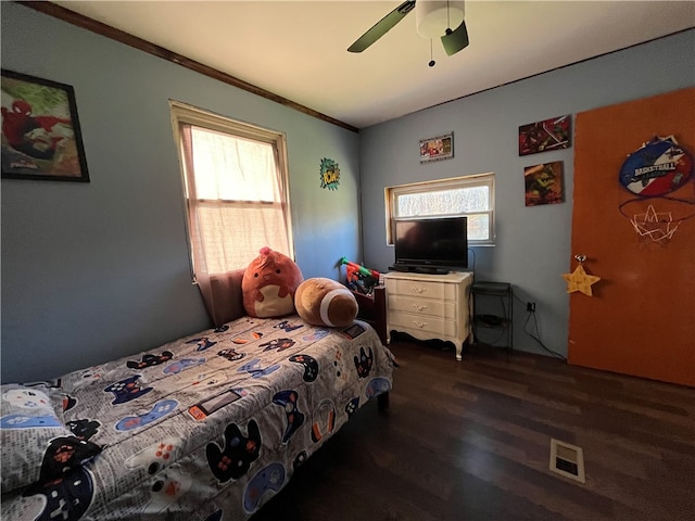 bedroom featuring dark wood-type flooring, ornamental molding, multiple windows, and ceiling fan