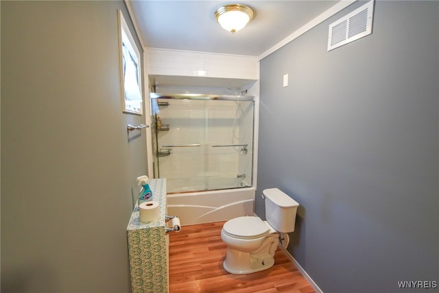 bathroom featuring ornamental molding, hardwood / wood-style flooring, toilet, and combined bath / shower with glass door