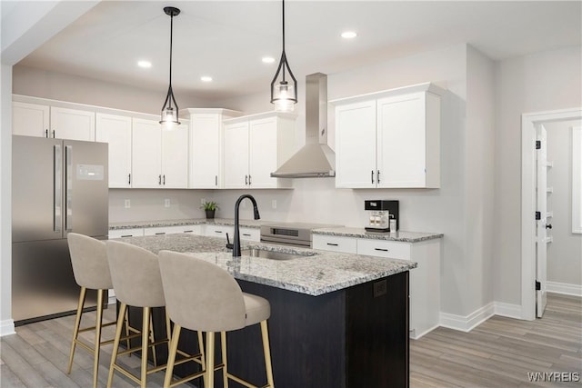 kitchen featuring stainless steel refrigerator, sink, white cabinets, and wall chimney range hood