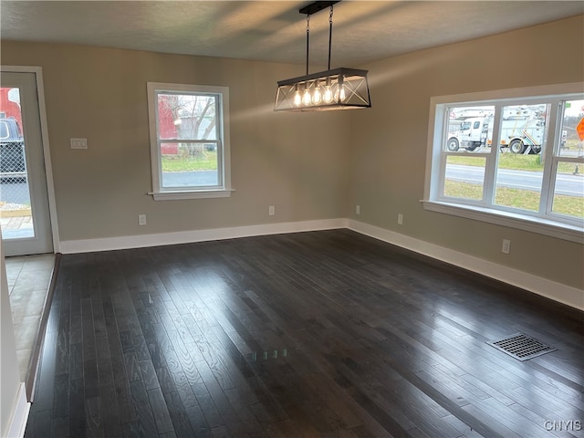 unfurnished dining area with a textured ceiling, plenty of natural light, dark wood-type flooring, and a chandelier