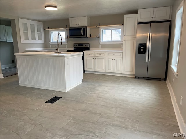 kitchen with stainless steel appliances, a center island with sink, a textured ceiling, sink, and white cabinetry