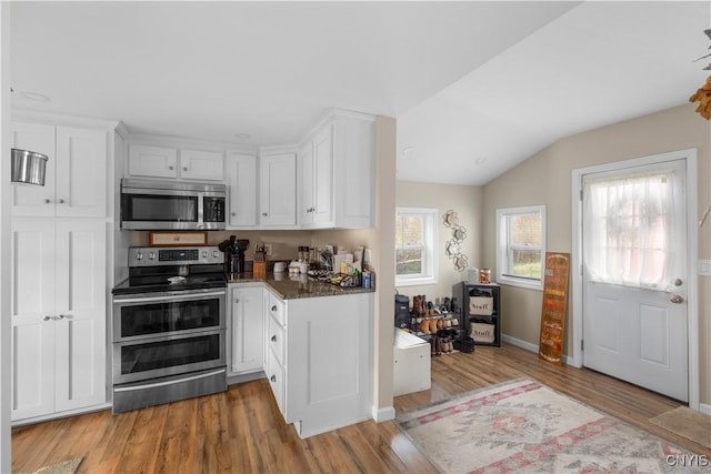 kitchen featuring white cabinetry, wood-type flooring, vaulted ceiling, appliances with stainless steel finishes, and dark stone counters