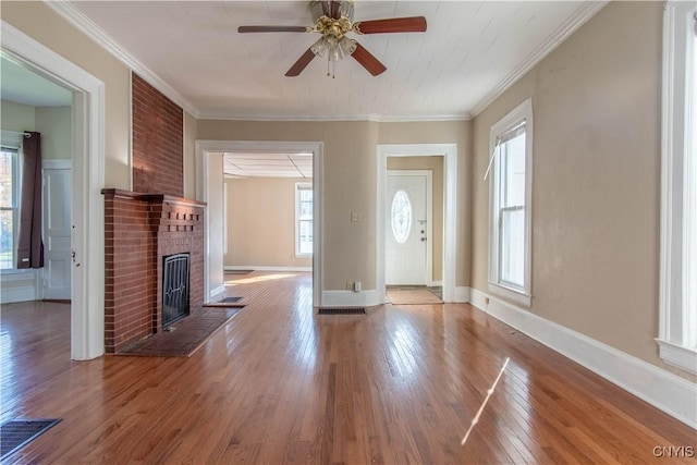 unfurnished living room with ceiling fan, a healthy amount of sunlight, crown molding, and a brick fireplace