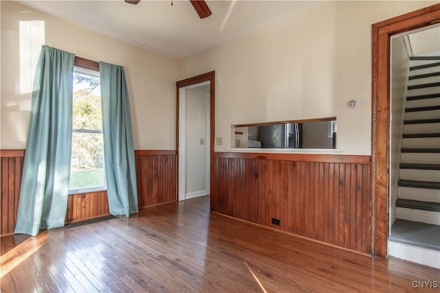 interior space with stainless steel fridge, hardwood / wood-style floors, ceiling fan, and wooden walls